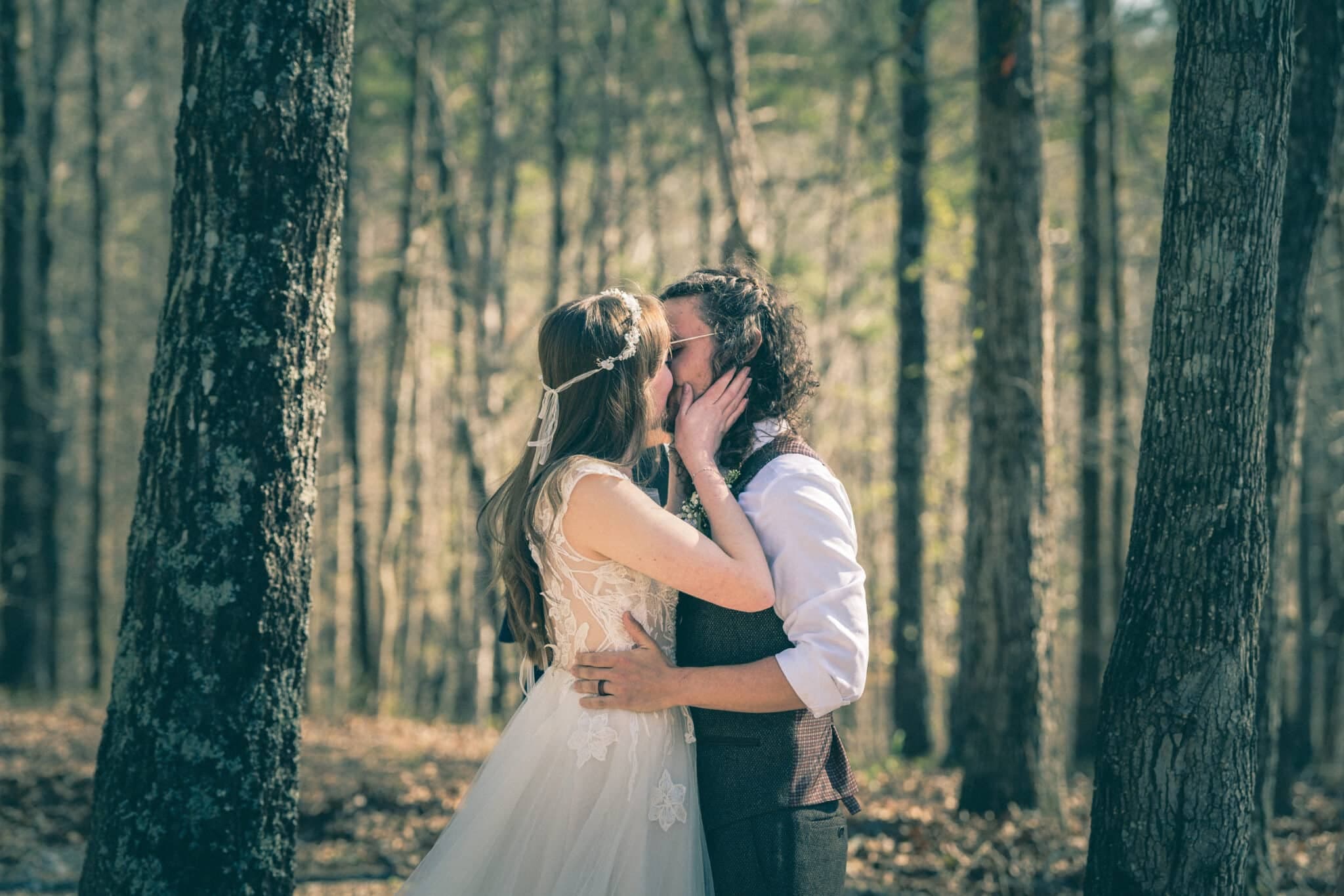 A couple in wedding attire embraces and shares a kiss in a wooded area. A couple in wedding attire embraces and shares a kiss in a wooded area.