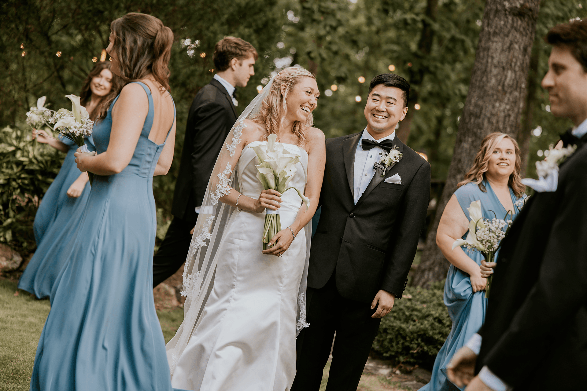 A smiling bride and groom share a joyful moment surrounded by their wedding party in a scenic outdoor setting. A smiling bride and groom share a joyful moment surrounded by their wedding party in a scenic outdoor setting.
