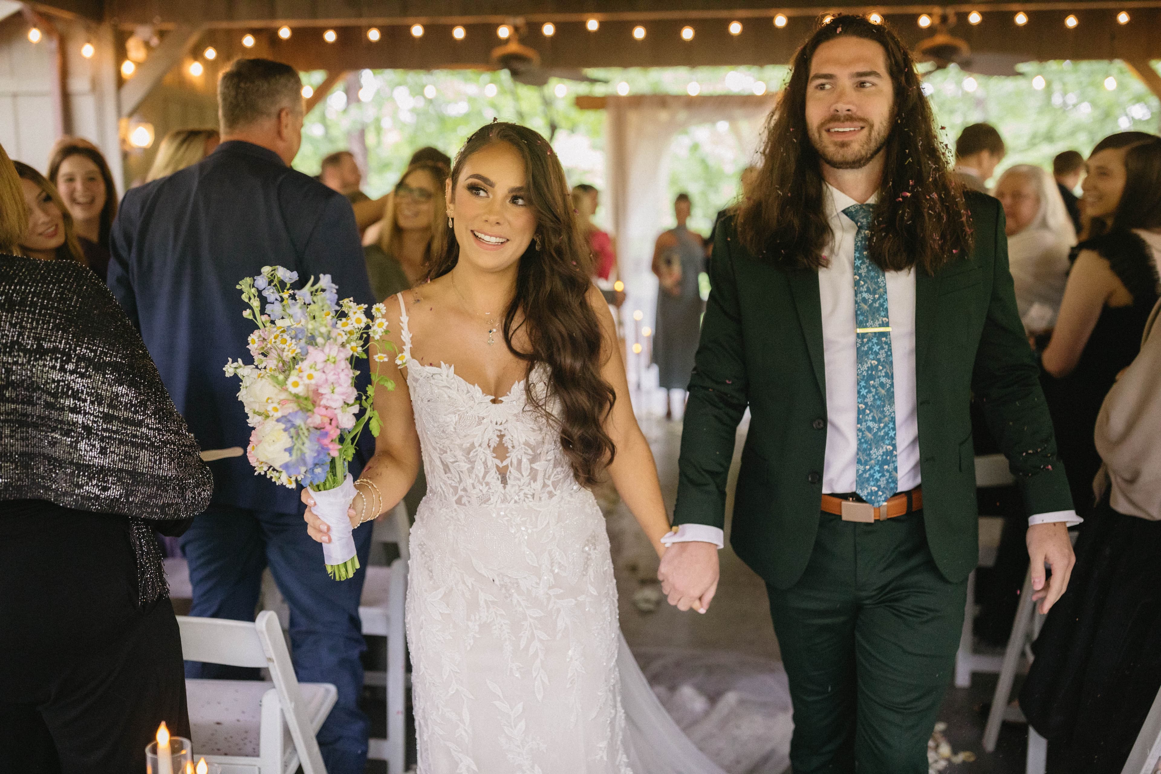 A bride and groom joyfully walk hand in hand down the aisle, surrounded by wedding guests.