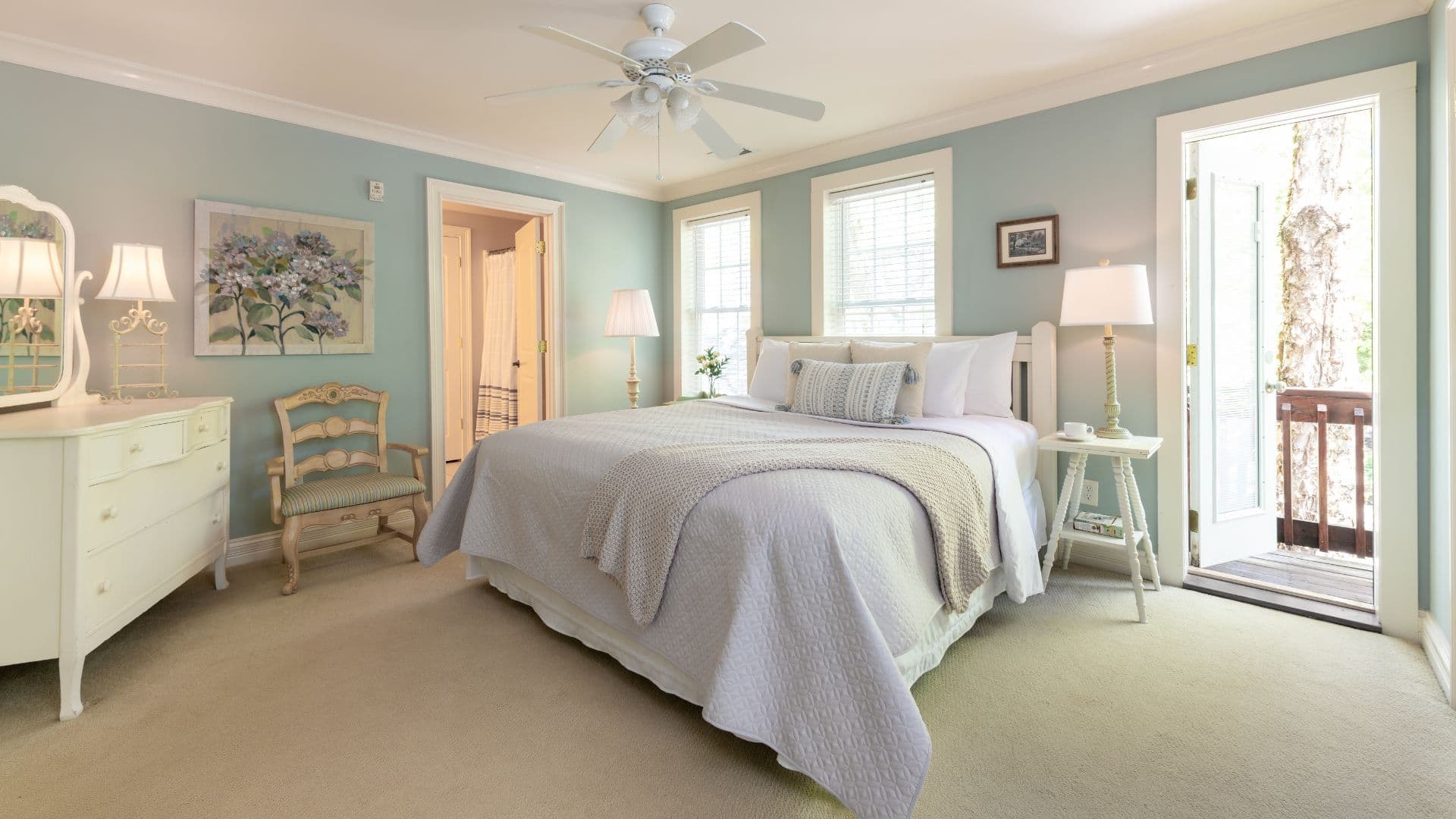 A bright and inviting bedroom with a queen-sized bed, a vintage chair, and glass doors leading to a small balcony.