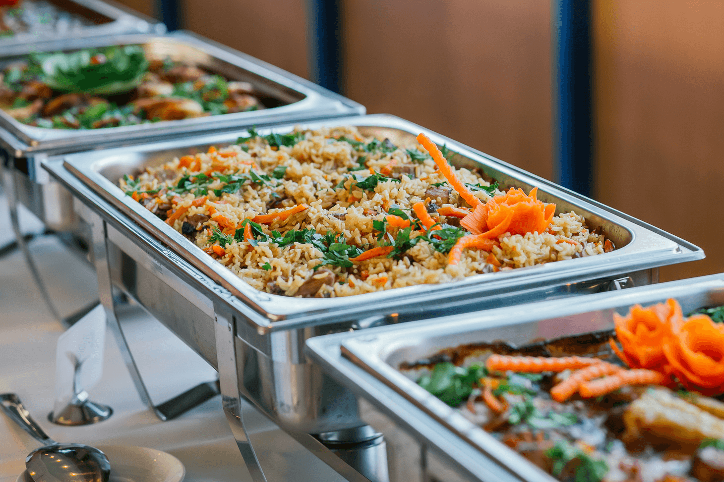 A buffet table featuring a selection of dishes, including vibrant rice topped with herbs and garnished with carrots.