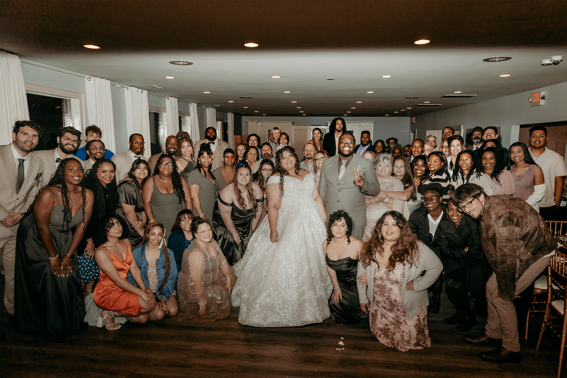 A large group of wedding guests gathers together for a photo, with the bride and groom prominently in the center. A large group of wedding guests gathers together for a photo, with the bride and groom prominently in the center.