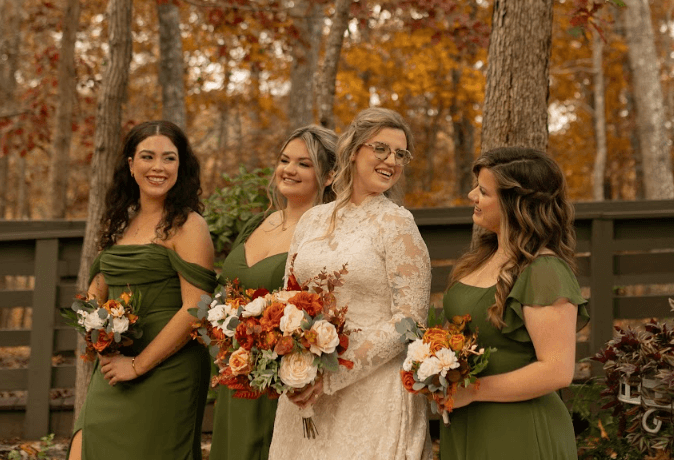 A bride in a white lace dress stands joyfully with four bridesmaids in green dresses, holding colorful floral bouquets in an autumn setting. A bride in a white lace dress stands joyfully with four bridesmaids in green dresses, holding colorful floral bouquets in an autumn setting.