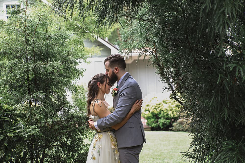 A couple embraces under lush greenery, sharing an intimate moment.
