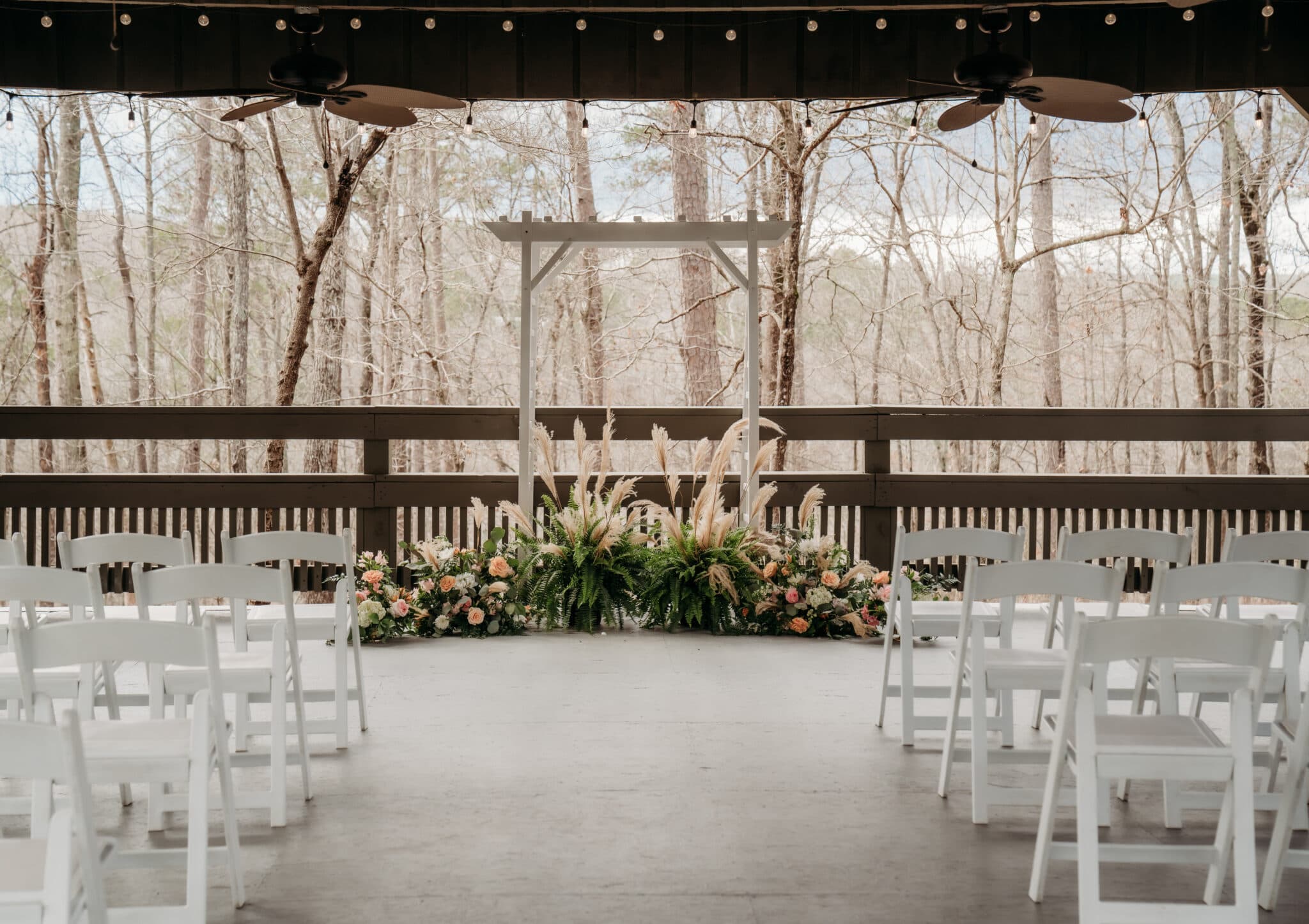 A decorated outdoor wedding ceremony space with floral arrangements and white chairs, set against a wooded backdrop. A decorated outdoor wedding ceremony space with floral arrangements and white chairs, set against a wooded backdrop.