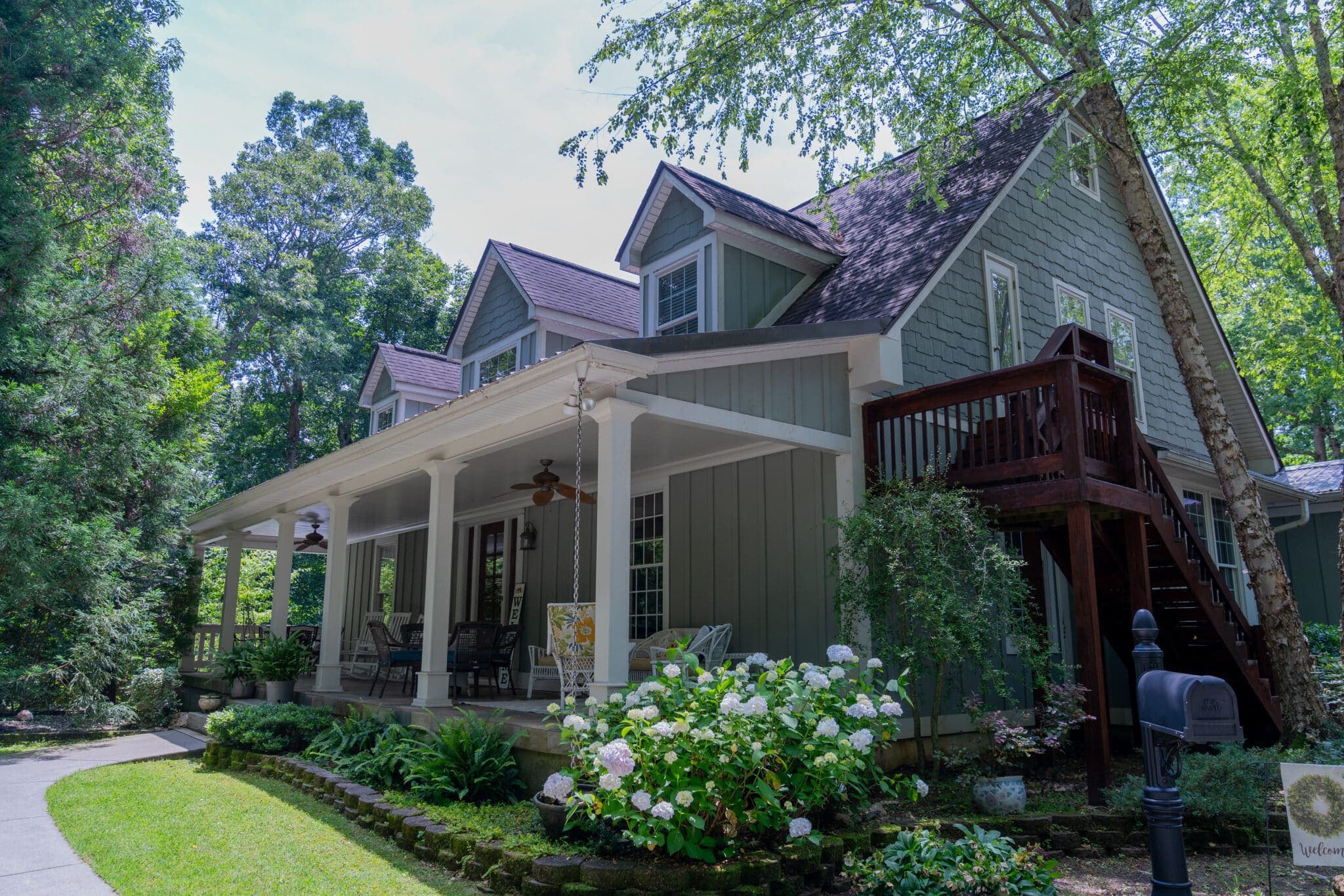 A charming gray house with a porch, surrounded by greenery and flowers.