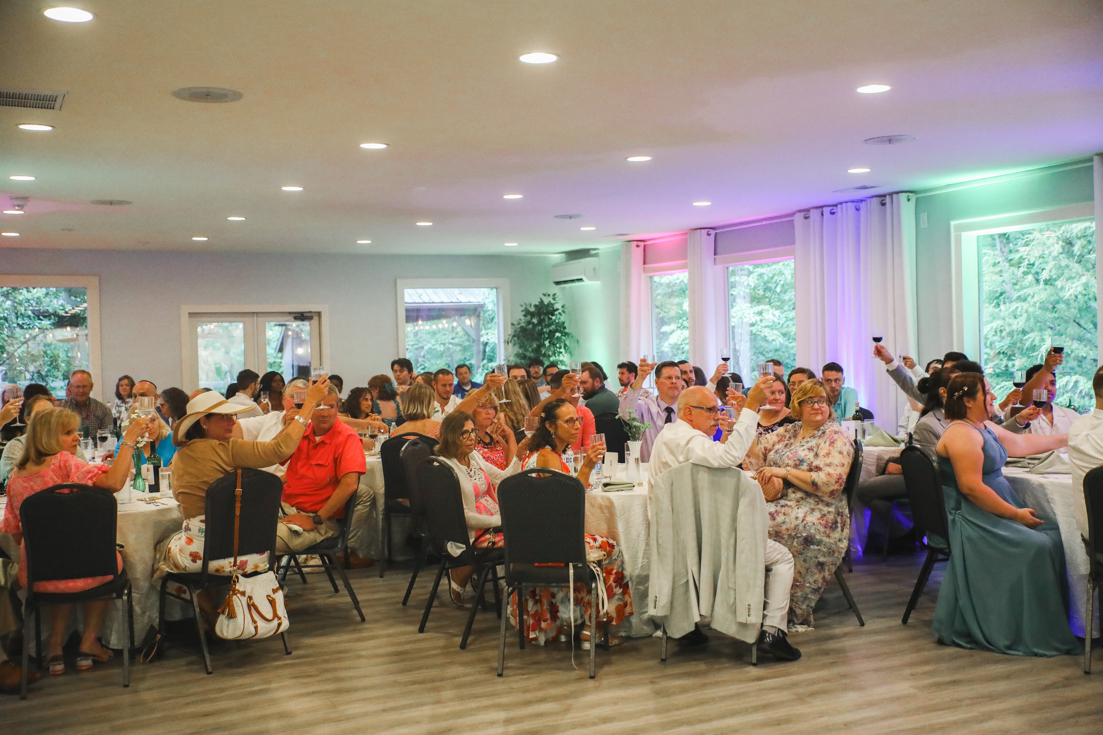 A large group of people raising glasses in a festive indoor setting with tables and decorations.