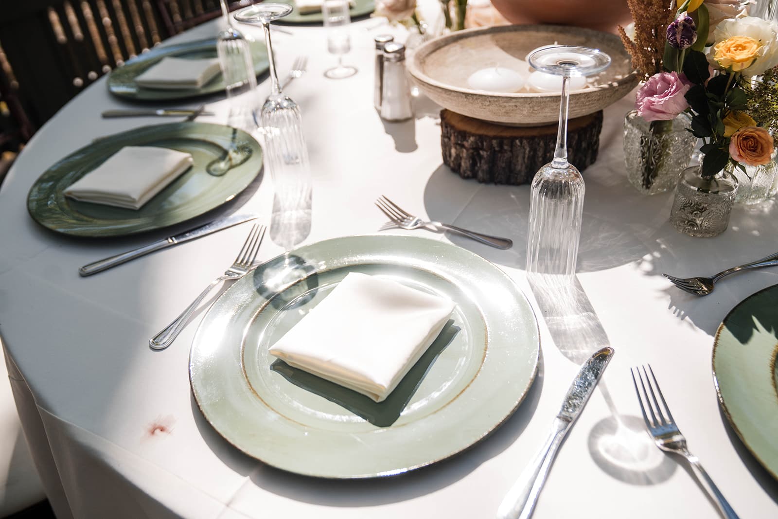 A beautifully set table with green plates, folded napkins, glasses, and silverware.