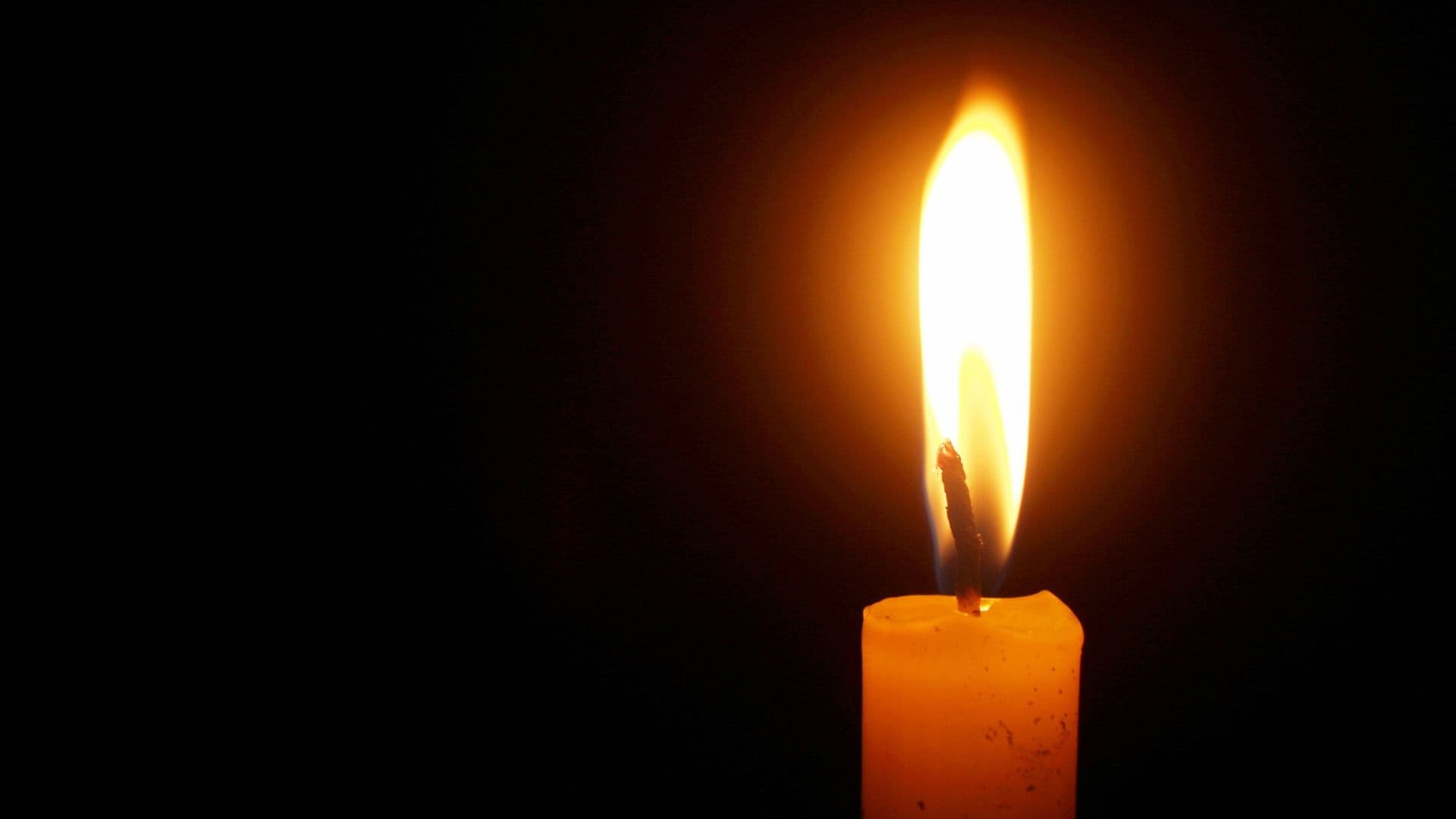 A lit candle flickers against a dark background. A lit candle flickers against a dark background.