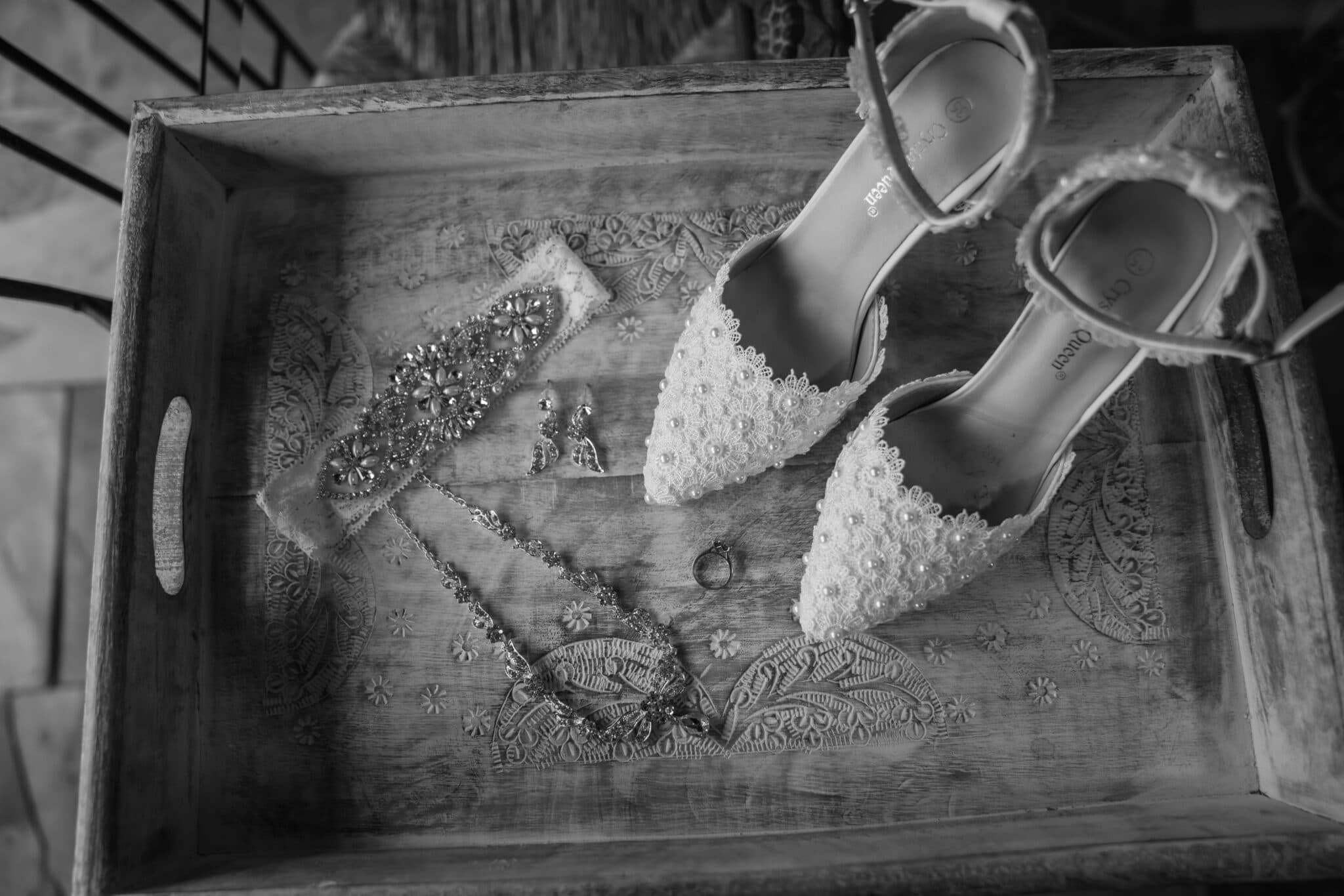 A wooden tray holds a pair of beaded white heels, a decorative hairpiece, earrings, and a necklace. A wooden tray holds a pair of beaded white heels, a decorative hairpiece, earrings, and a necklace.