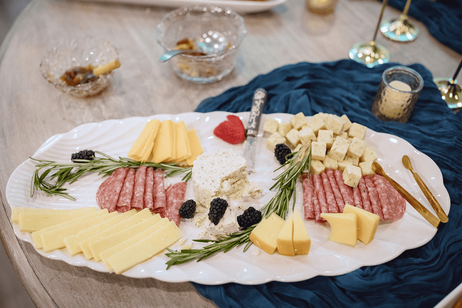 A beautifully arranged charcuterie platter featuring various cheeses, sliced meats, blackberries, and garnished with fresh rosemary.