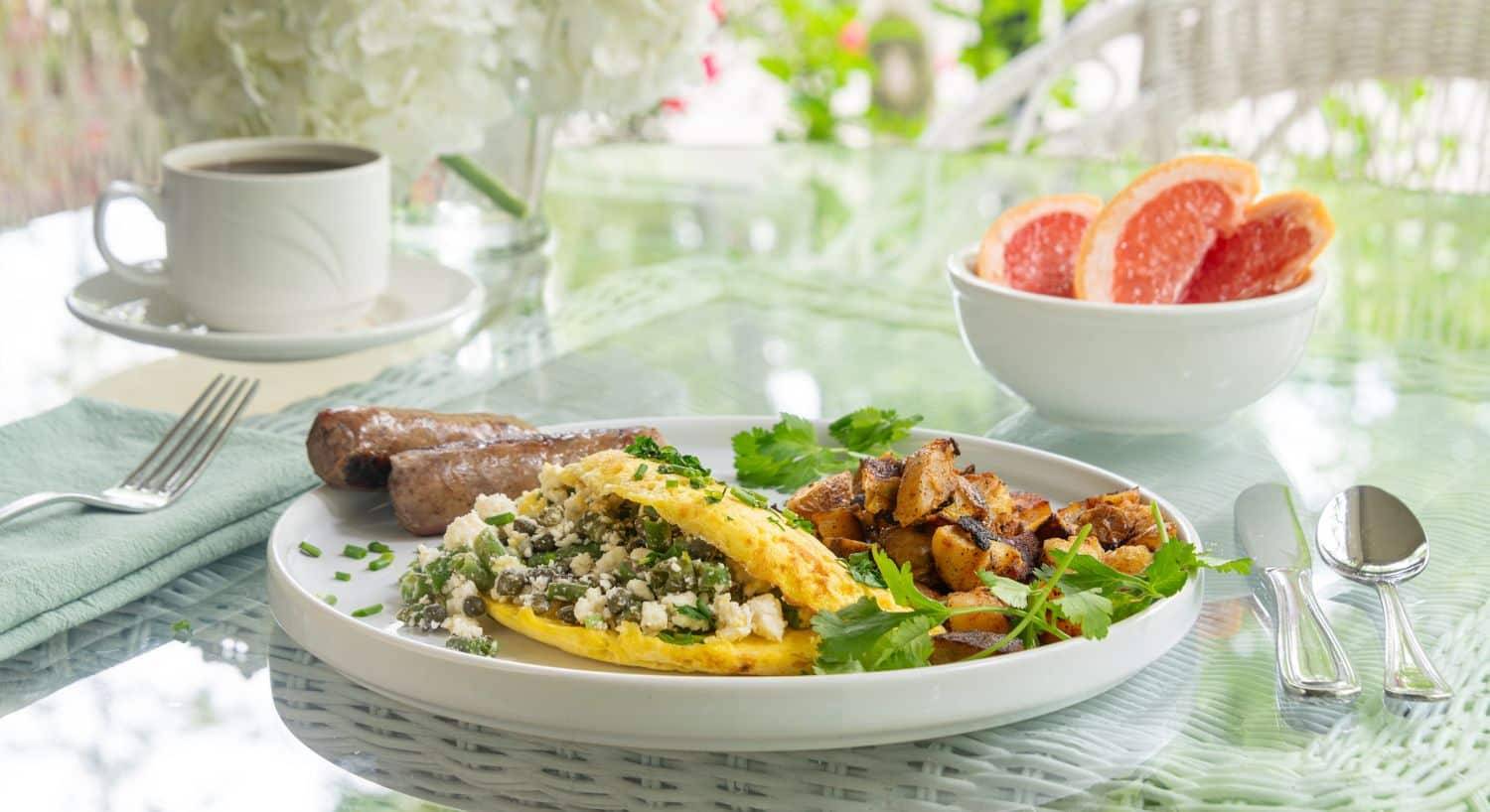 Glass table with breakfast plate; omelette, sausage links, potatoes and bowl of sliced grapefruit